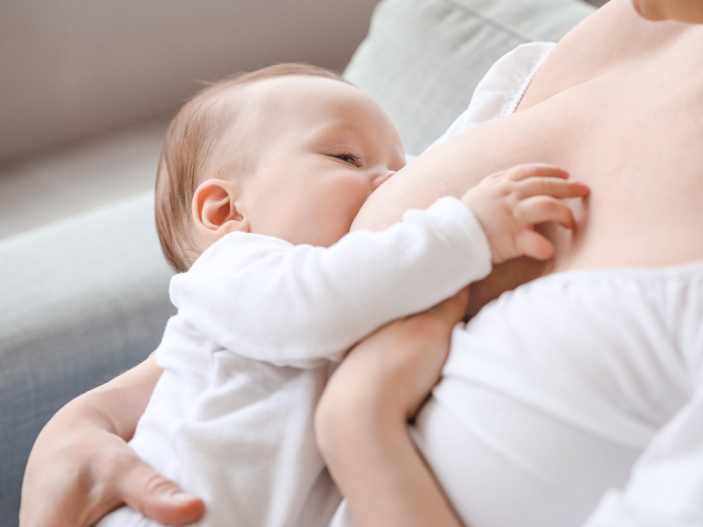 Infant breastfeeding, cradled in a caregiver’s arms, latched to the breast.
